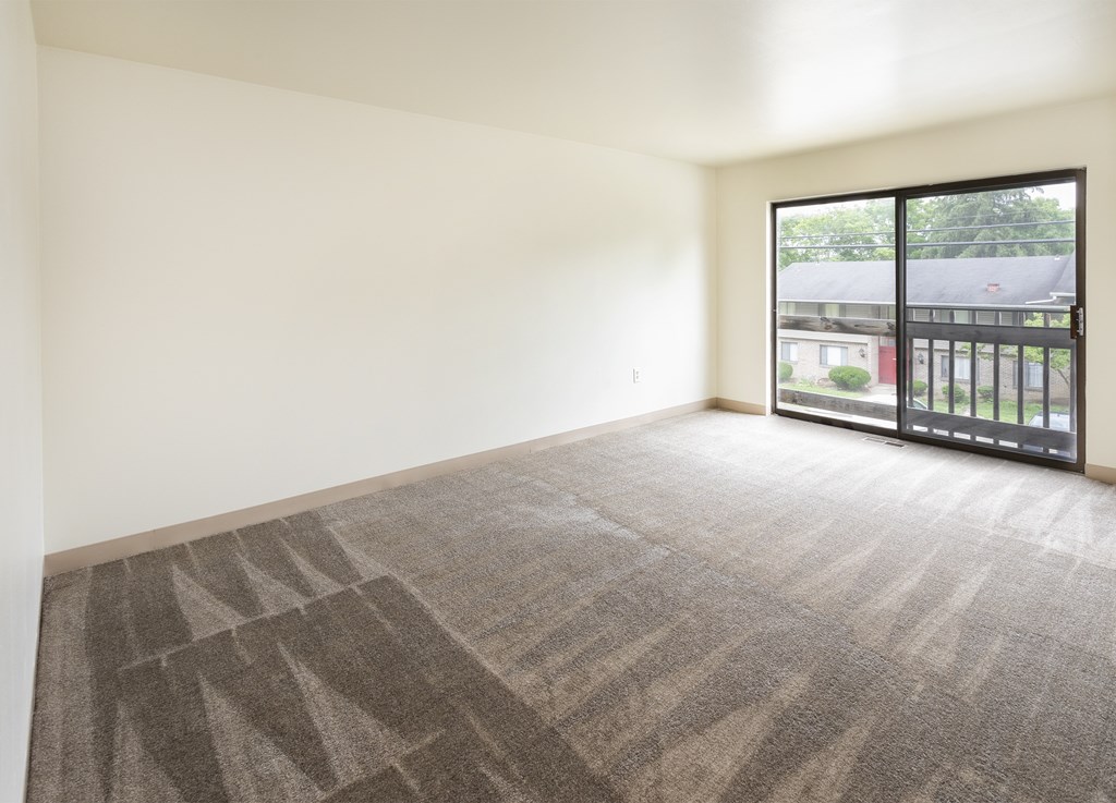 A room with a carpeted floor and a large window with a view of a parking lot.