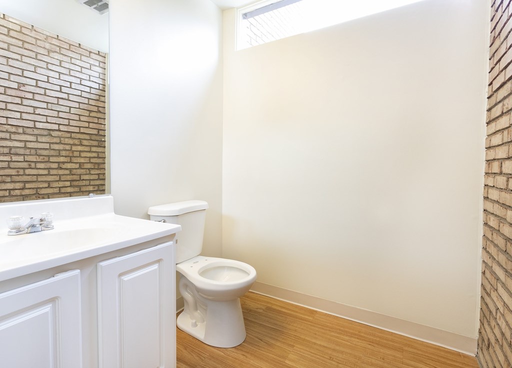 A white toilet sits in a bathroom with a brick wall.