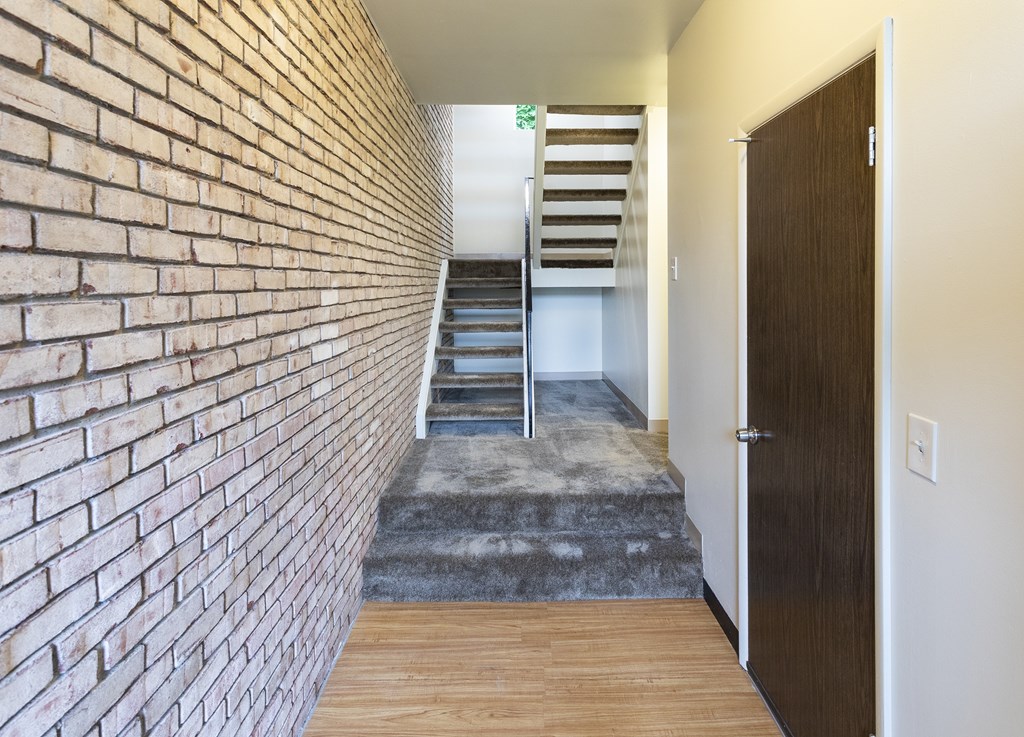 A hallway with a brick wall on the left and a wooden door on the right.