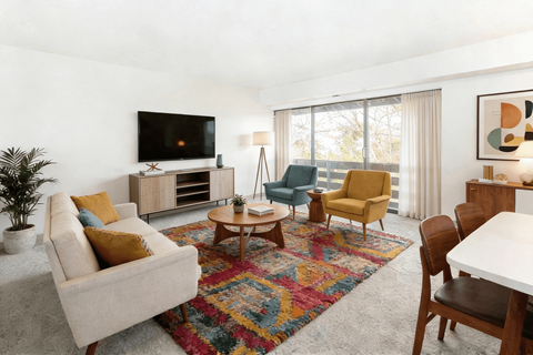 A living room with a white couch, a coffee table, a chair, a television, and a potted plant.