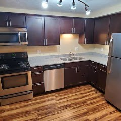 A kitchen with dark brown cabinets and wooden floors.