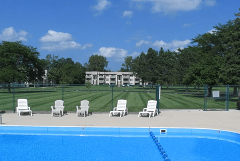 A pool with chairs around it and a building in the background.