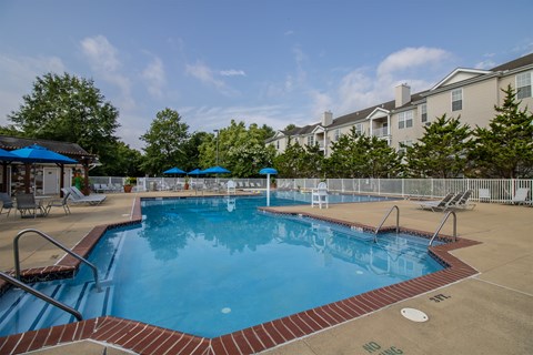 A large outdoor swimming pool with a red brick border and a blue umbrella.