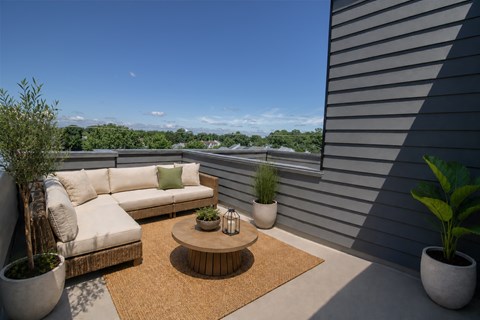 A patio with a white couch, a coffee table, and potted plants.