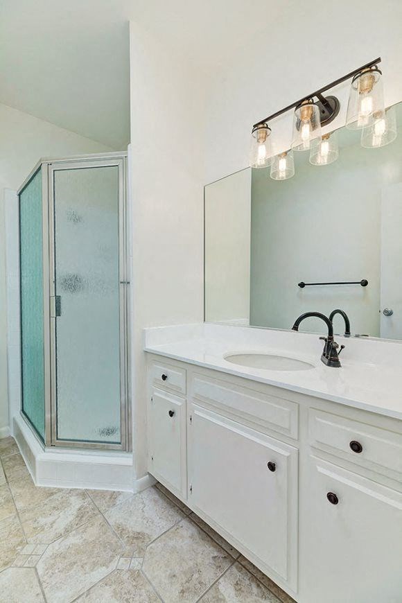 White counter top, new vanity faucet, lighting, and shower enclosure