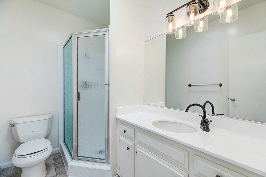 White vanity counter top and new light fixture over vanity adjacent toilet and shower enclosure