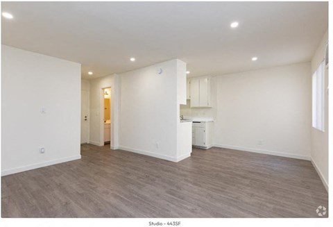a living room and kitchen with white walls and wood floors