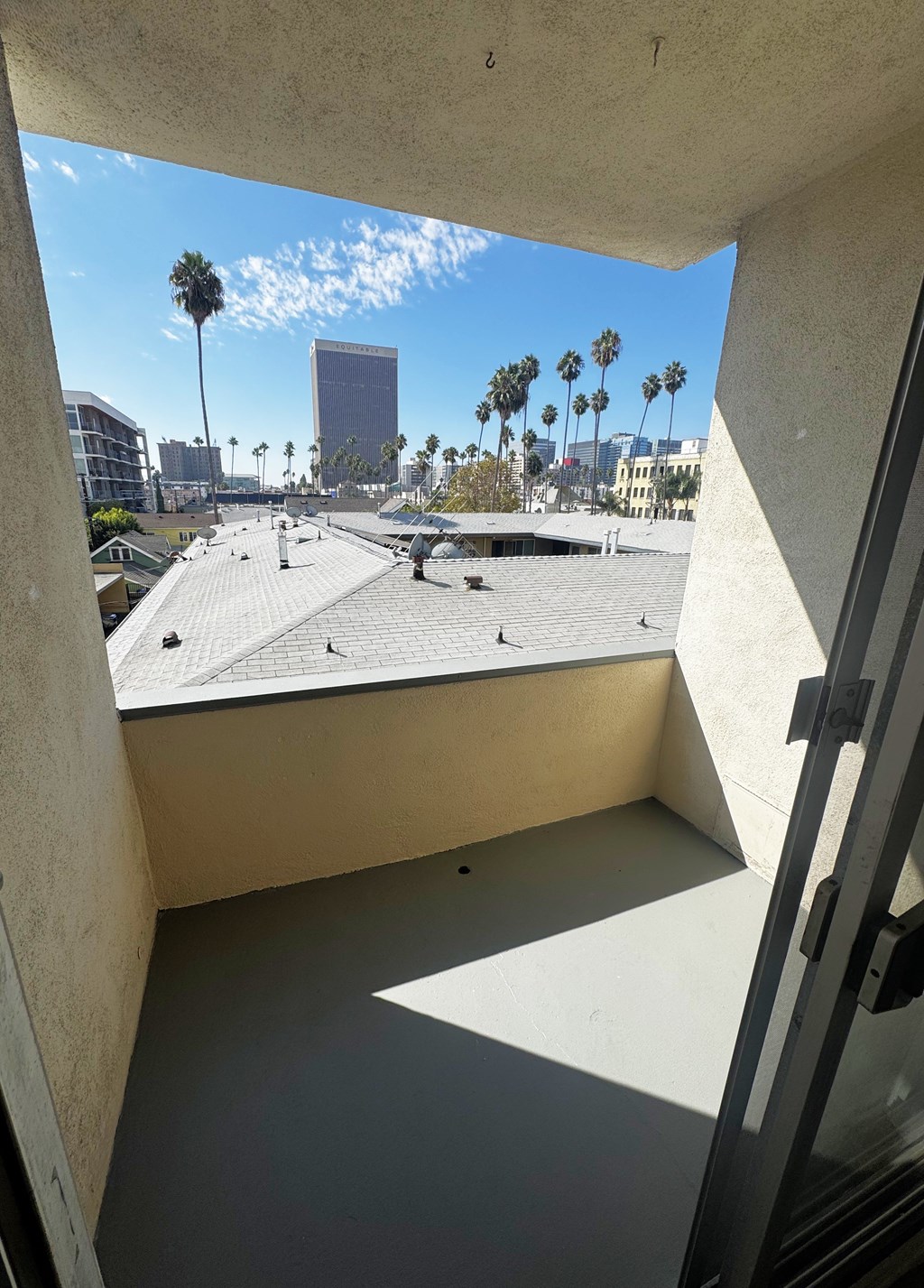 A view from a window looking out at a rooftop with palm trees and buildings in the distance.