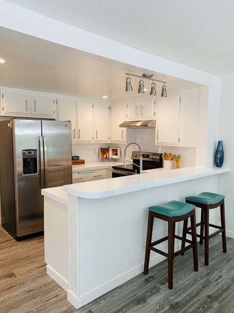 a kitchen with white cabinets and a bar with three stools
