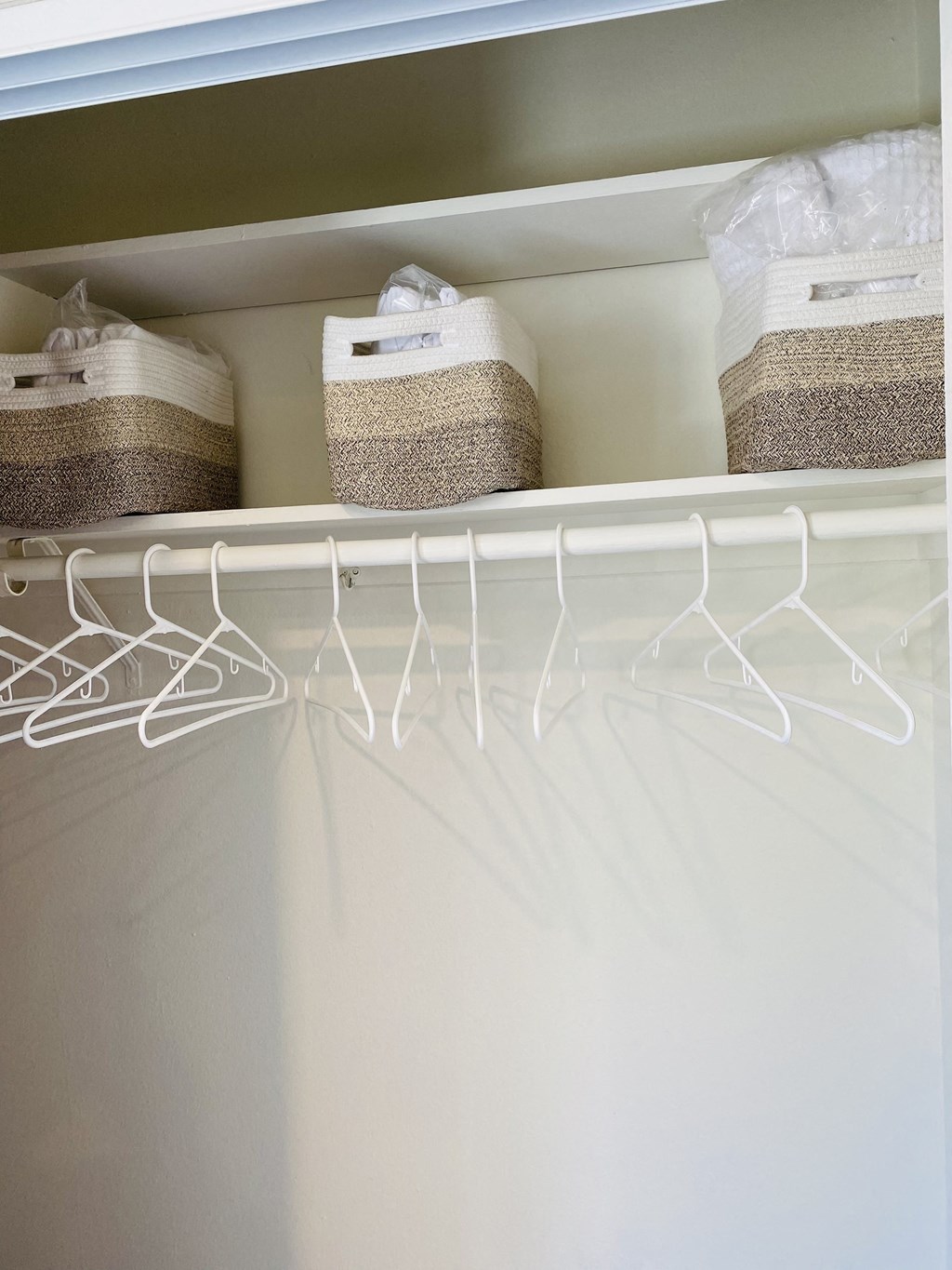 a white closet with baskets and hangers on the shelf