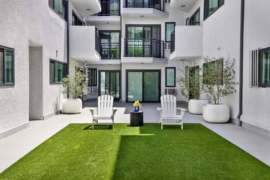 A white patio with two chairs and a table with a vase of flowers on it.