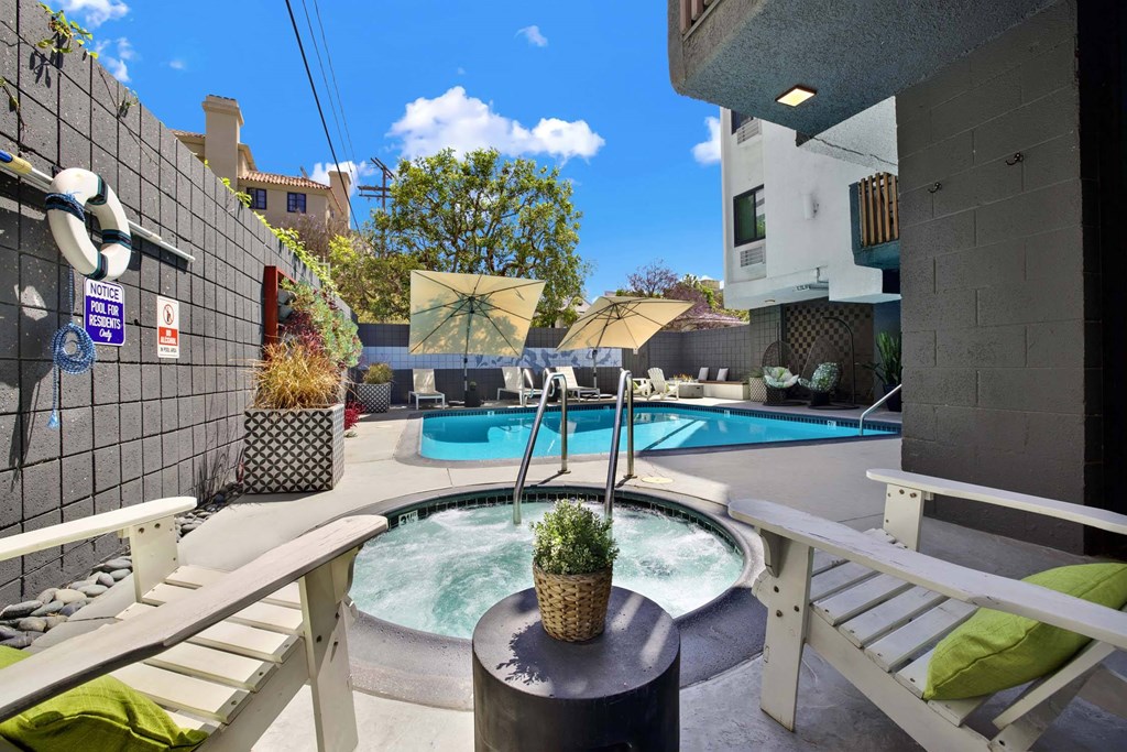 A hot tub sits in the middle of a patio with a white bench and a black table.