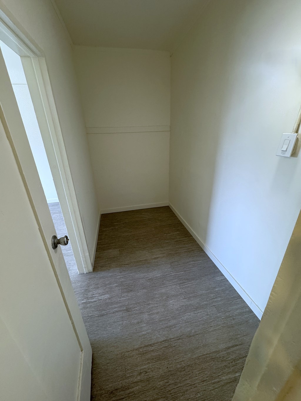 A hallway with a door on the left and a light switch on the wall.