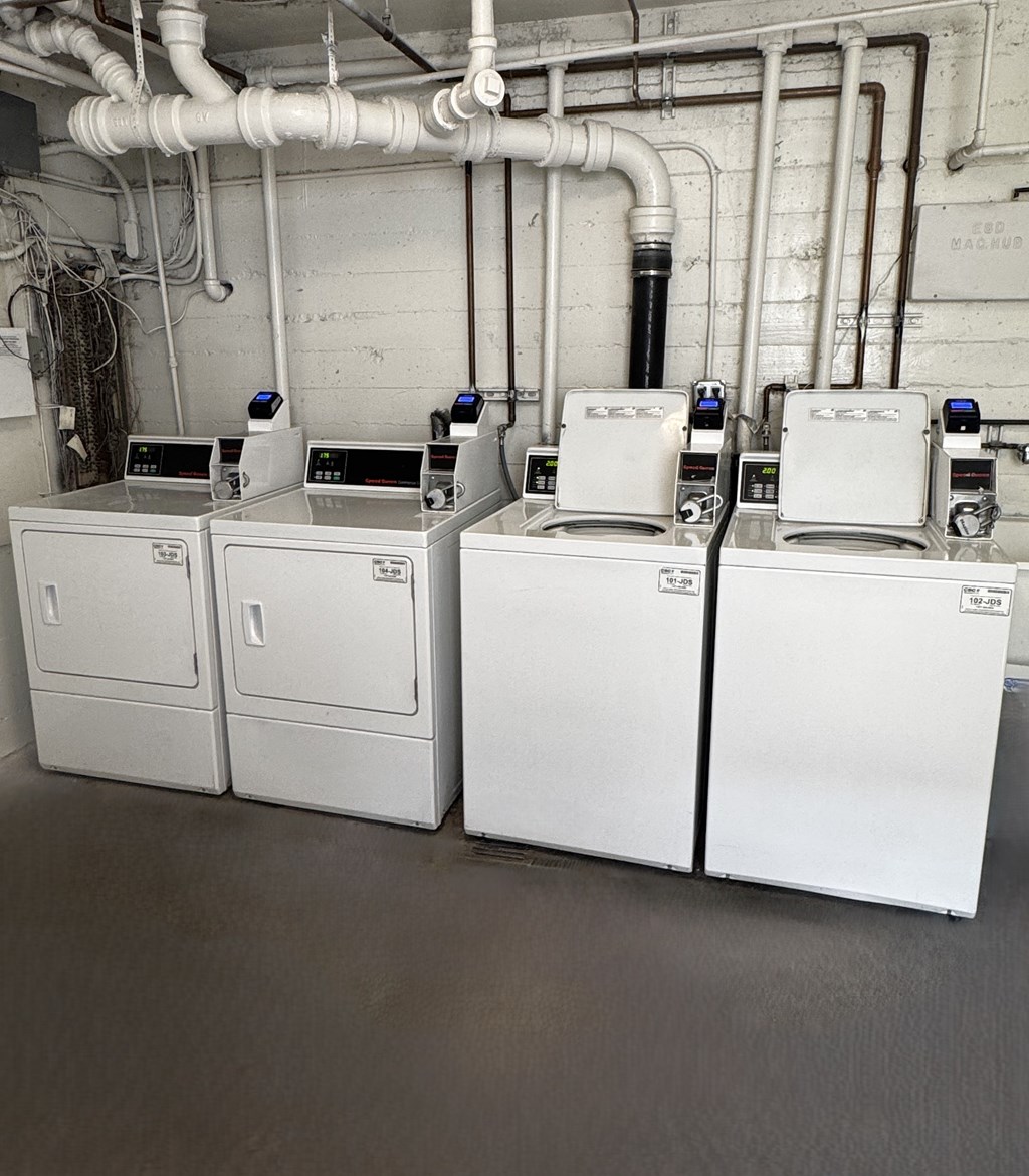 A row of white industrial machines are lined up in a room with white walls and pipes.