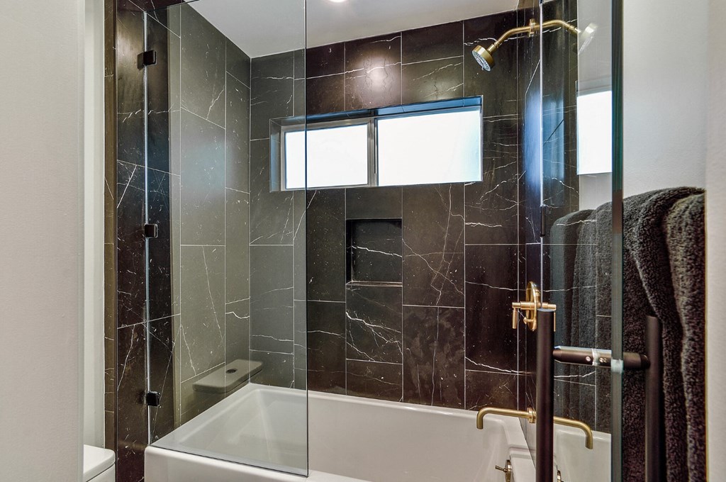 a bathroom with black tile and a shower and a tub