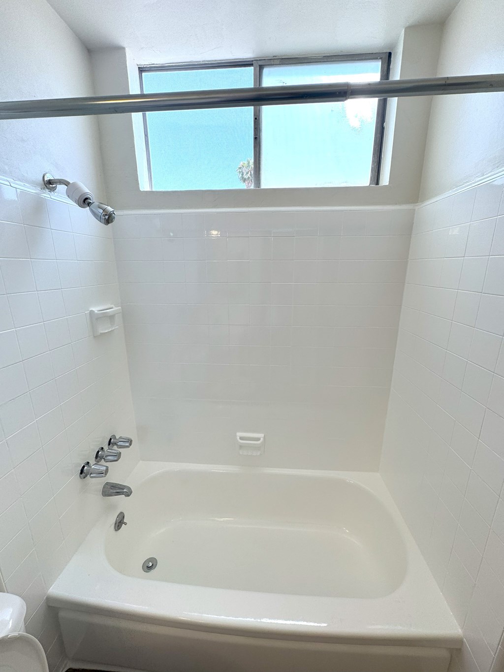 A white bathtub with a window above it.