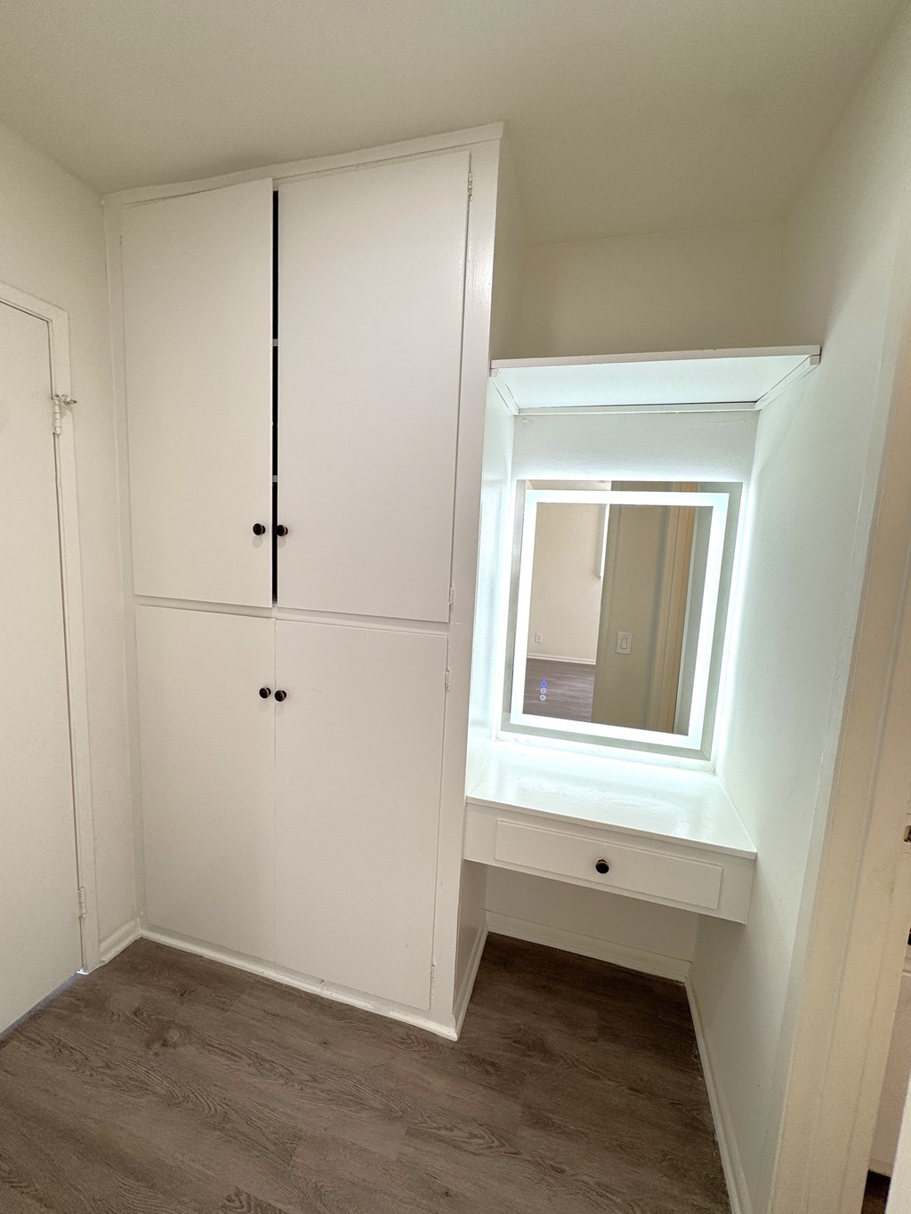 A white wardrobe with a mirror and a small drawer is in a room.