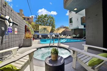 A hot tub sits in the middle of a patio with a white bench on either side.