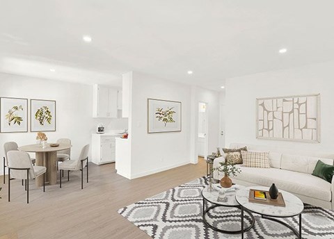A living room with a white couch, a dining table with chairs, and a rug on the floor.