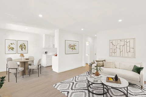 A living room with a white couch, a dining table with chairs, and a rug on the floor.