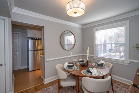 A dining room with a table set for two and a refrigerator in the background.