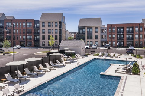 A swimming pool surrounded by sun loungers and umbrellas in front of a building.