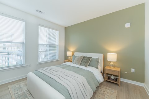 A bedroom with a large windows, LVT flooring, tall ceilings and modern finishes.