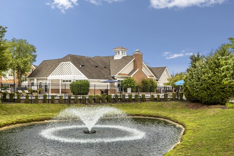 A fountain in the middle of a pond in front of a house.