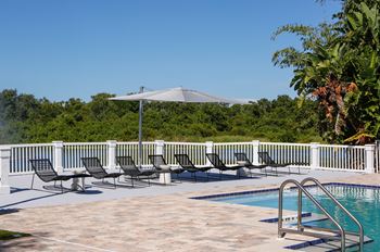 a swimming pool with black lounge chairs and an umbrella at Champions Walk Apartment Homes, Florida
