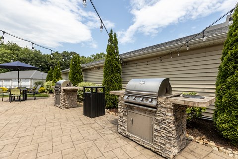 A stone BBQ grill is in the middle of a patio.
