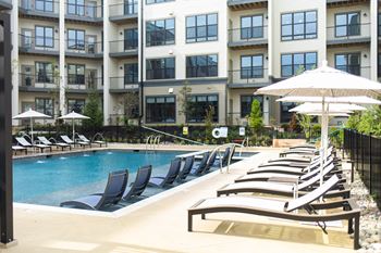 a pool with lounge chairs and an umbrella in front of an apartment building at The Yards at Malvern, Pennsylvania, 19355