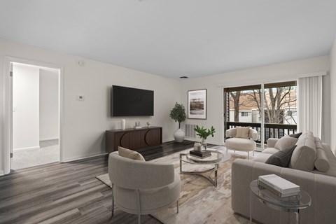 A living room with a grey sofa, a white armchair, a glass coffee table, and a television on the wall.