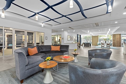 A grey couch with orange pillows sits in a room with a glass wall.