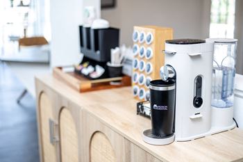 A coffee maker is on a wooden countertop with a white and black coffee maker to its right.