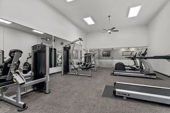 A well-equipped gym with a variety of machines and a fan on the ceiling.