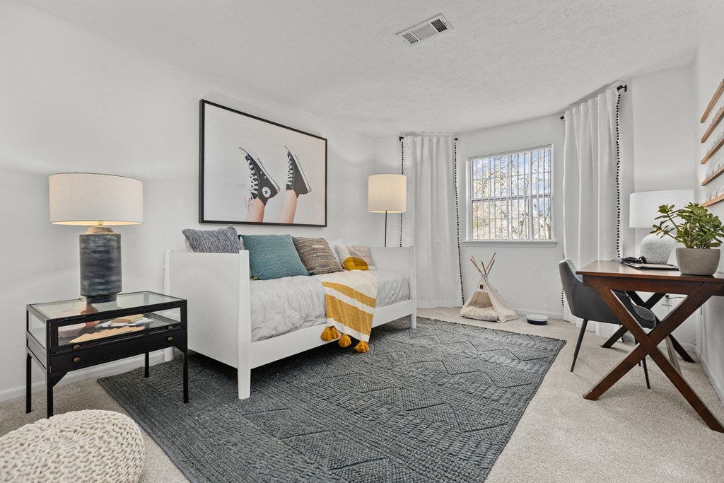 A modern bedroom with a white bed, a glass table, and a rug on the floor.