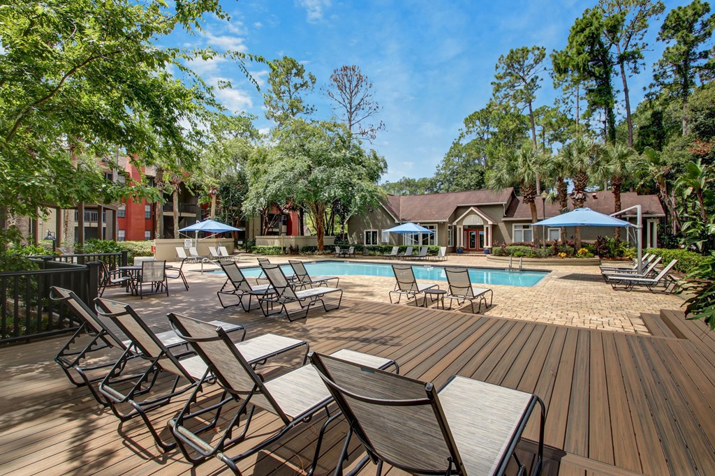 A pool surrounded by chairs and trees.