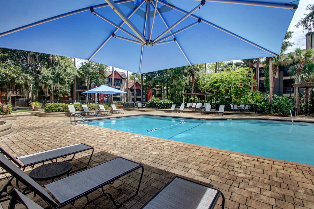 A pool surrounded by a patio with chairs and umbrellas.