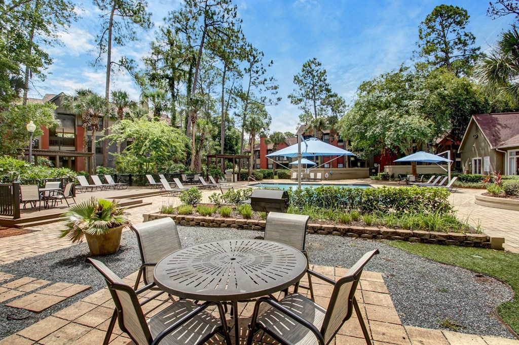 A patio with a table and chairs is surrounded by greenery.