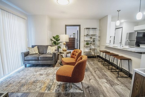 A living room with a grey couch, a grey rug, a brown chair and a white fridge.