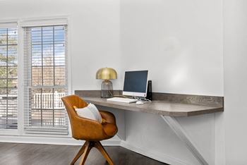 A brown chair is in front of a desk with a laptop and a lamp on it.