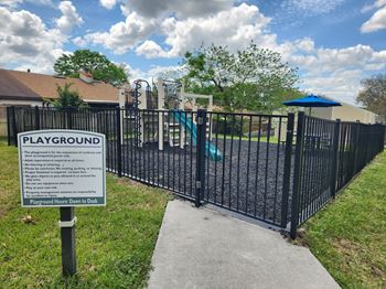 A sign on a playground gate provides information about the playground's rules and regulations.