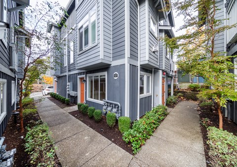 a sidewalk in front of a gray building with a bench