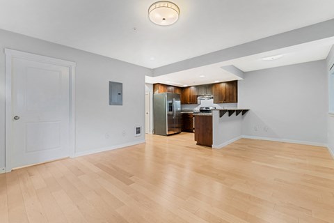 the living room and kitchen of an apartment with a hardwood floor and white walls