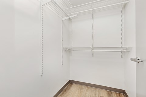 a room with white walls and wood flooring and a white closet with white shelves
