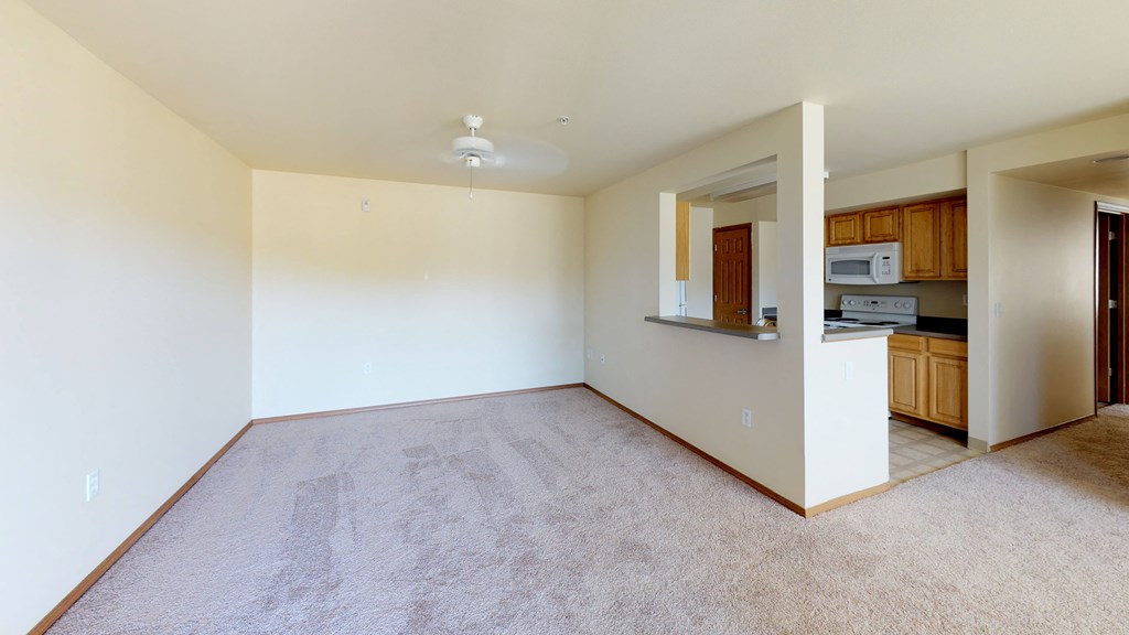 an empty living room with a kitchen in the corner