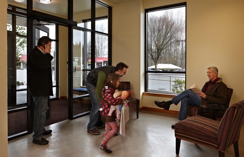A man is reading a book while a little girl stands in front of him.