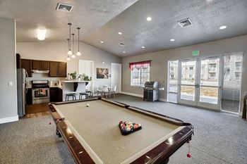 A pool table is in the middle of a room with a kitchen area in the background.