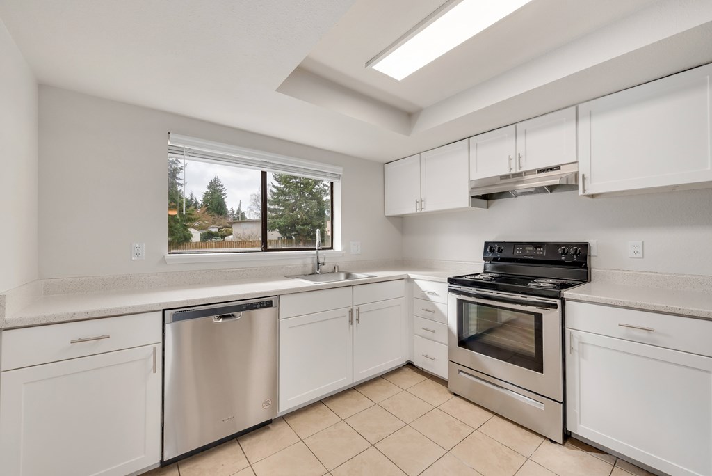 A kitchen with white cabinets and appliances, a stainless steel dishwasher, and a stove top oven.