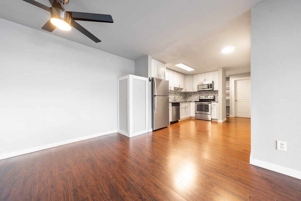 an empty living room with wood flooring and a kitchen